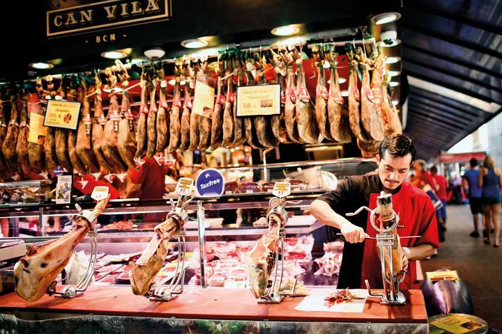 Auf dem Mercat de la Boqueria werden unzäh­­lige Delikatessen angeboten, so hängen auch Schinken vom Pata-Negra-Schwein an den Haken. / © Shutterstock